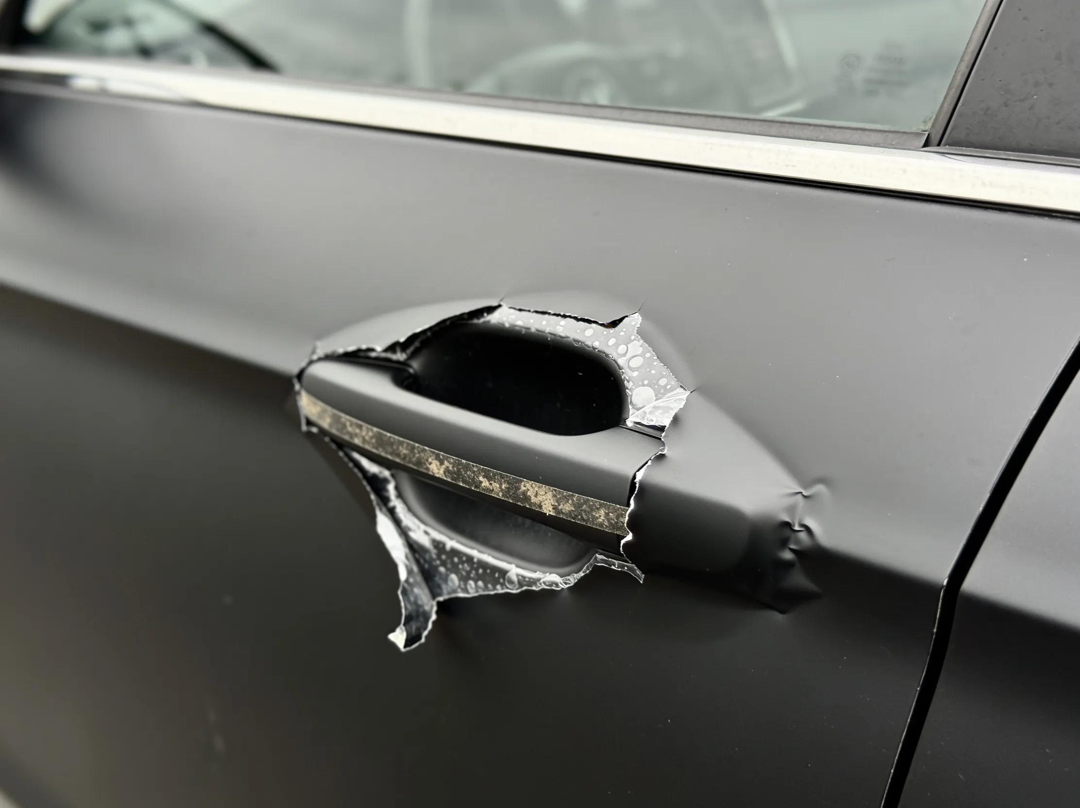 Overstretched vinyl wrap tearing away around a car door handle